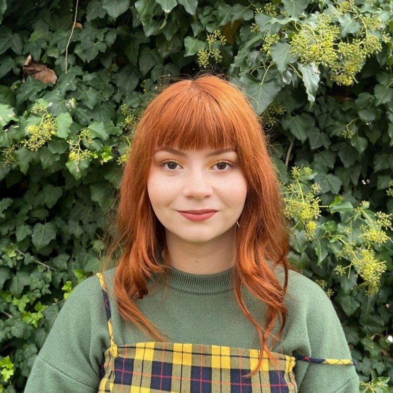 Sofía Gil, con pelo colorado y flequillo, sonriendo frente a una pared de hiedra